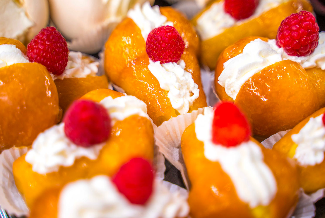 Assortimento di deliziosi babà artigianali farciti con ciuffi di soffice panna montata e guarniti con lamponi freschi, una specialità della Pasticceria Martinangeli (Le Dolci Tradizioni).