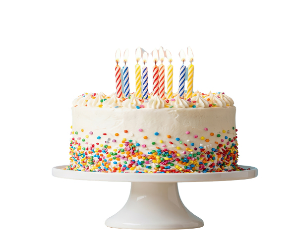 Torta di compleanno artigianale con copertura di panna bianca, decorata con un'abbondante cascata di confettini colorati e diverse candeline accese, presentata su un'alzata bianca e realizzata dalla Pasticceria Martinangeli (Le Dolci Tradizioni).