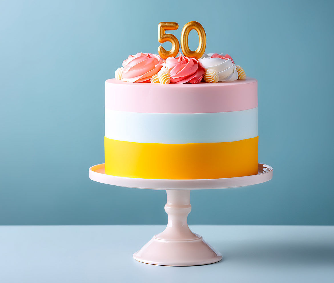 Raffinata torta celebrativa a strati colorati nelle tonalità del rosa, bianco e giallo, decorata con soffici ciuffi di panna e un topper dorato con il numero 50, realizzata artigianalmente dalla Pasticceria Martinangeli (Le Dolci Tradizioni) per occasioni speciali.