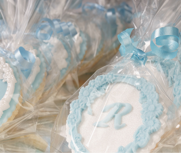 Biscotti artigianali decorati con glassa bianca e azzurra, caratterizzati dalla lettera "R" al centro e confezionati singolarmente in sacchetti trasparenti chiusi da un nastro azzurro.