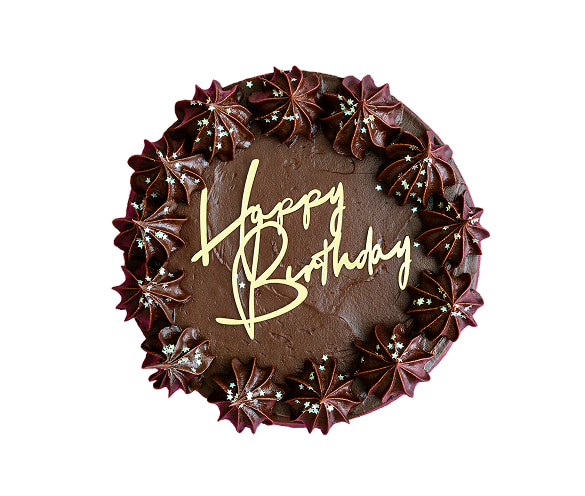 Vista dall'alto di una torta artigianale al cioccolato decorata con una corona di ciuffi di crema con stelline argentate e un topper dorato con la scritta "Happy Birthday", realizzata dalla Pasticceria Martinangeli (Le Dolci Tradizioni).